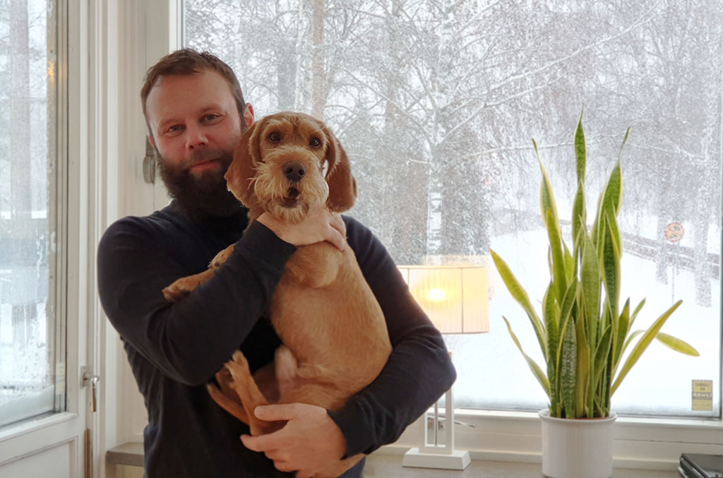 Pelle står framför fönstret på sitt kontor på faluvägen. Han håller hunden Peanut i famnen. Utanför fönstret snöar det.